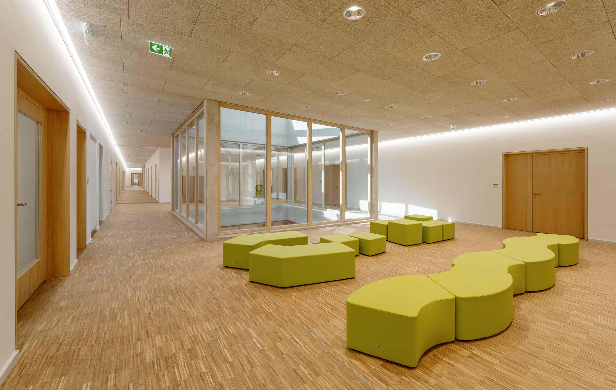 Aufenthaltsbereich mit grünen Sitzmöbeln – Grundschule Haar: Erweiterung, Turnhalle und Tiefgarage