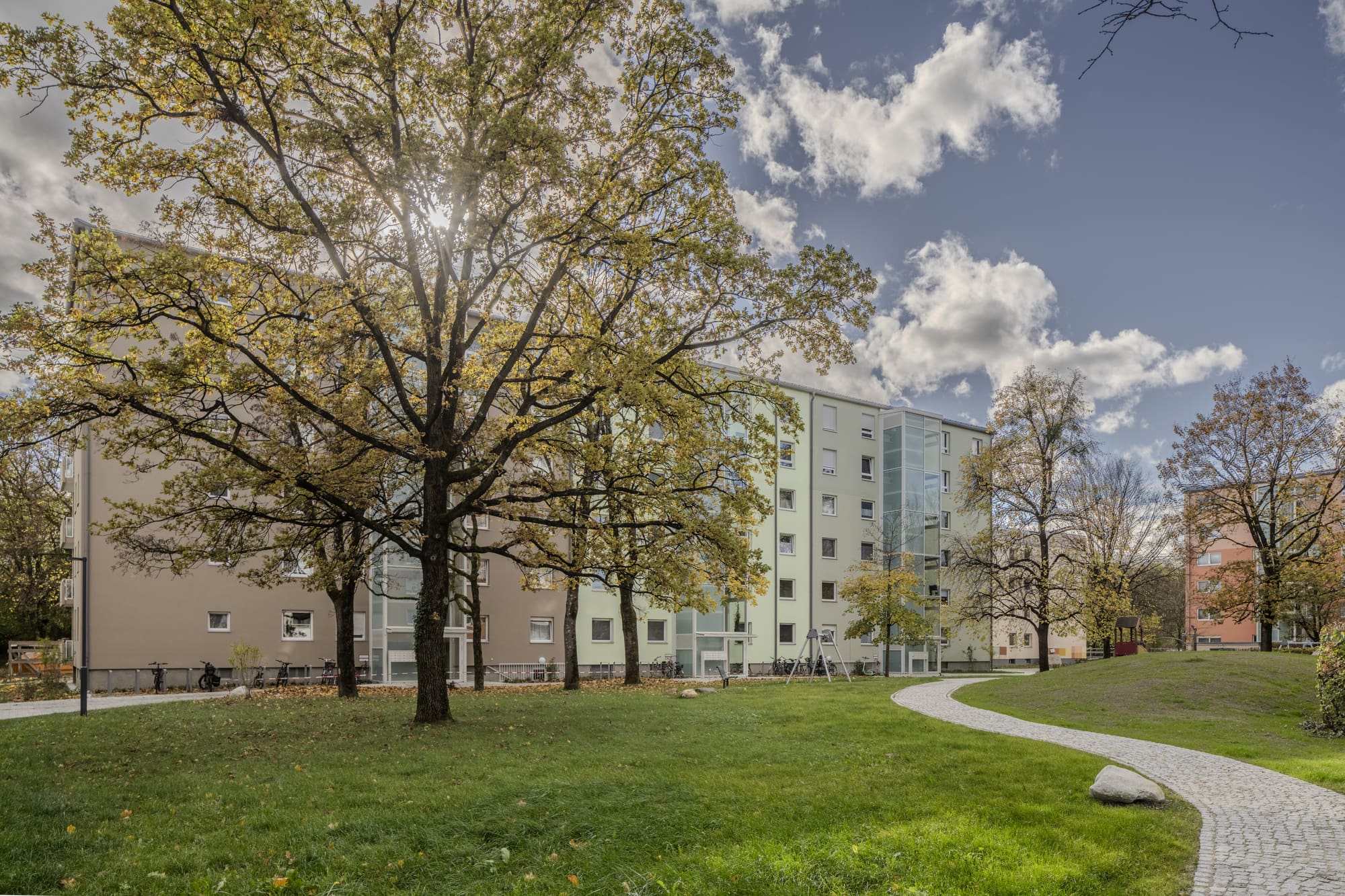 Wohnanlage hinter altem Baumbestand – Nachverdichtung und Aufstockung in München
